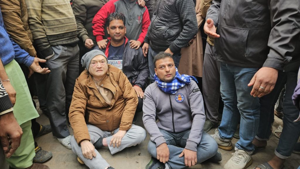 जेसीबी के सामने बैठे लोग